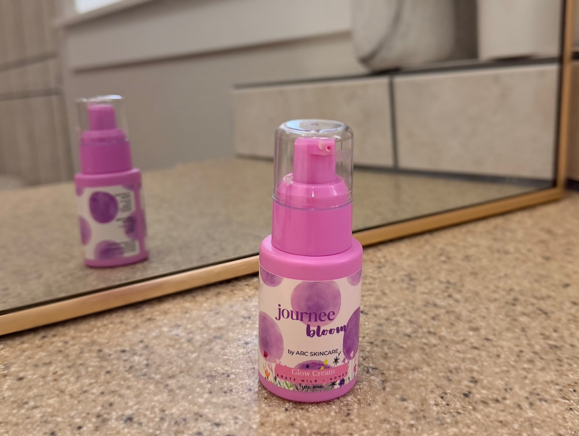 Pink bottle labeled 'journee bloom' on a bathroom counter with mirror reflection.